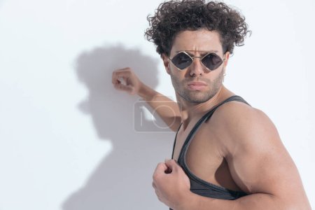 Photo for Arab man with curly hair in undershirt looking away while laying on a grey wall - Royalty Free Image