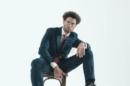 Photo for Portrait of handsome businessman posing with relaxed stance, sitting, wearing eyeglasses against gray studio background - Royalty Free Image