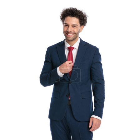 Photo for Portrait of happy businessman with curly hair adjusting tie and smiling in front of white background in studio - Royalty Free Image