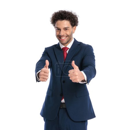Téléchargez les photos : Portrait d'homme d'affaires élégant faisant le pouce vers le haut geste et souriant devant fond blanc en studio - en image libre de droit