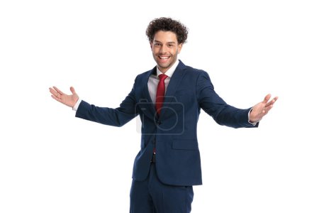 Foto de Proud young man in elegant suit opening arms and welcoming, smiling and being happy in front of white background in studio - Imagen libre de derechos