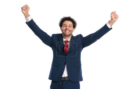 Téléchargez les photos : Excited young businessman with curly hair holding fists in the air, being enthusiastic and laughing in front of white background in studio - en image libre de droit