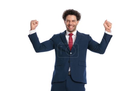 Photo pour Cheerful young man in elegant suit with fists up celebrating the victory in front of white background in studio - image libre de droit
