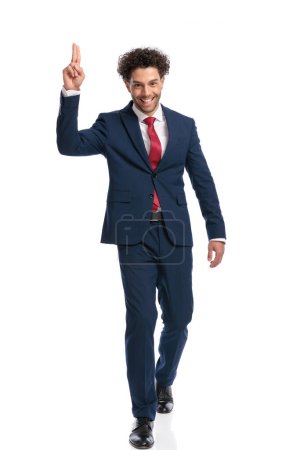 Photo for Elegant young businessman holding fingers up, smiling and walking in front of white background in studio - Royalty Free Image