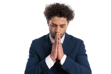 Photo for Lebanese young man in elegant suit being spiritual, closing eyes and praying in front of white background in studio - Royalty Free Image