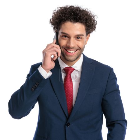 Foto de Feliz joven empresario teniendo una conversación telefónica y sonriendo delante de fondo blanco en el estudio - Imagen libre de derechos