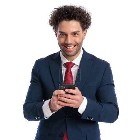 Téléchargez les photos : Portrait of happy young businessman reading messaged and smiling in front of white background in studio - en image libre de droit