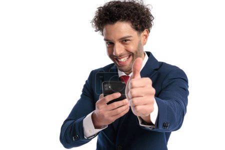Photo for Curly hair turkish man scrolling on social media and making thumbs up gesture while smiling and laughing on white background in studio - Royalty Free Image
