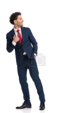 Téléchargez les photos : Homme arrabique attrayant avec la main dans la poche regardant vers le côté et marchant devant fond blanc en studio - en image libre de droit