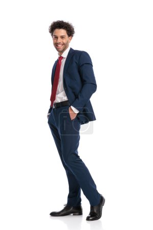 Photo for Full body picture of happy young businessman posing with hands in pockets and smiling in front of white background in studio - Royalty Free Image