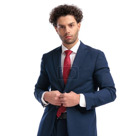 Téléchargez les photos : Portrait of sexy turkish businessman with curly hair buttoning navy blue suit and posing on white background in studio - en image libre de droit
