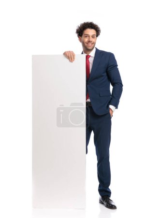 Photo for Confident elegant man in suit presenting white empty billboard and smiling on white background - Royalty Free Image
