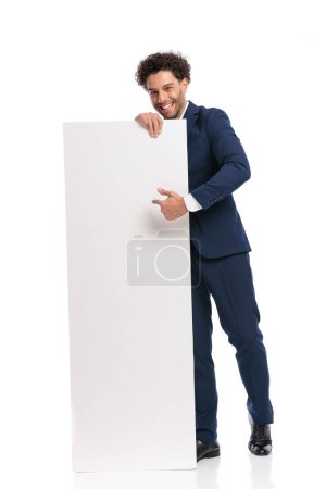 Photo for Full body picture of elegant businessman pointing finger to empty board in front of white background in studio - Royalty Free Image