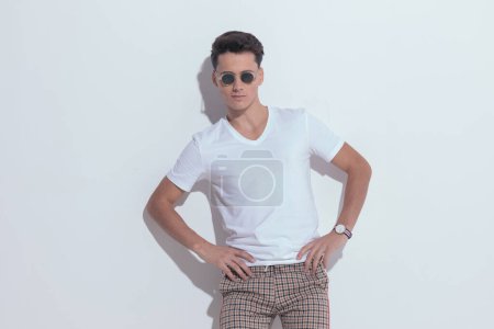 Photo for Portrait of  young casual man putting his hands on hips, standing, wearing sunglasses in a fashion pose - Royalty Free Image