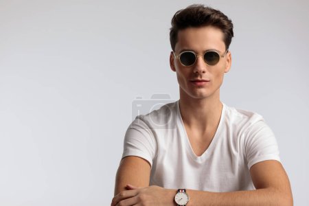 Photo for Portrait of young casual man with subtle smile is wearing cool sunglasses, sitting, wearing sunglasses in a fashion pose - Royalty Free Image