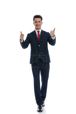 Foto de Young businessman walking and giving a thumbs up, wearing a suit and tie against white background - Imagen libre de derechos