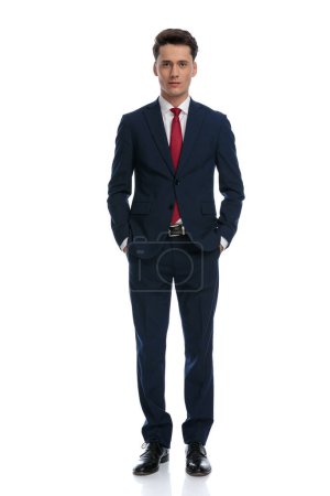 Foto de Hombre de negocios guapo poniendo sus manos en los bolsillos, vistiendo un traje y corbata contra fondo blanco - Imagen libre de derechos