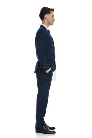 Téléchargez les photos : Handsome businessman waiting in line with hands in pockets, wearing a suit and tie against white background - en image libre de droit