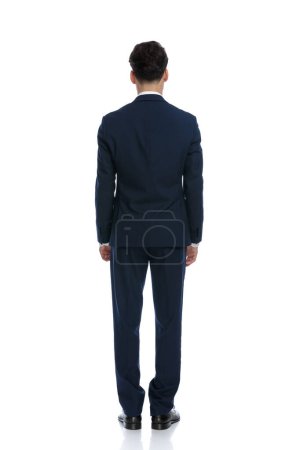 Téléchargez les photos : Young businessman turning his back at the camera, wearing a suit and tie against white background - en image libre de droit