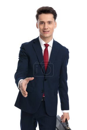 Téléchargez les photos : Attrayant homme d'affaires tenant la mallette et serrant la main, portant un costume et cravate sur fond blanc - en image libre de droit