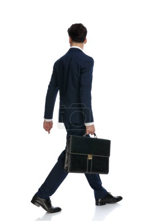 Téléchargez les photos : Bel homme d'affaires marchant, détournant les yeux et tenant la mallette, portant un costume et une cravate sur fond blanc - en image libre de droit