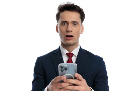 Foto de Handsome businessman texting on his phone and feeling shocked, wearing a suit and tie against white background - Imagen libre de derechos