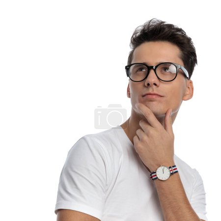 Foto de Retrato de hombre casual reflexivo en camisa blanca con gafas mirando hacia arriba y soñando delante de fondo blanco en el estudio - Imagen libre de derechos