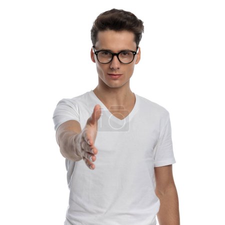 Téléchargez les photos : Beau jeune homme avec des lunettes tenant et serrant la main devant fond blanc en studio - en image libre de droit