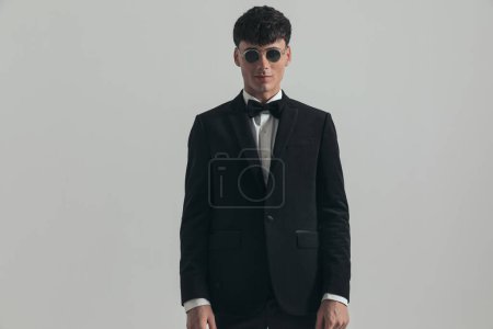 Photo for Portrait of attractive businessman posing with style, standing, wearing a black tuxedo and sunglasses, in a fashion pose - Royalty Free Image