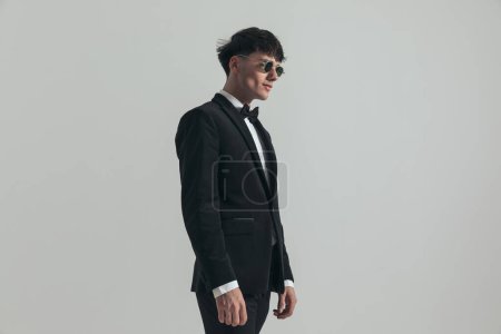 Photo for Portrait of young businessman posing like a badass, standing, wearing a black tuxedo and sunglasses, in a fashion pose - Royalty Free Image