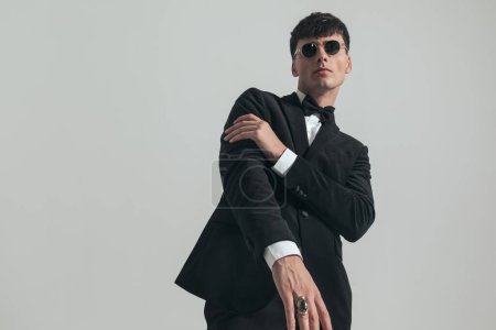 Foto de Portrait of handsome businessman with cool, shiny ring on his finger, standing, wearing a black tuxedo and sunglasses, in a fashion pose - Imagen libre de derechos