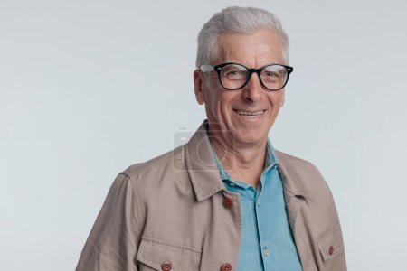 Téléchargez les photos : Portrait of old man with grey hair wearing glasses and laughing in front of grey background in studio - en image libre de droit
