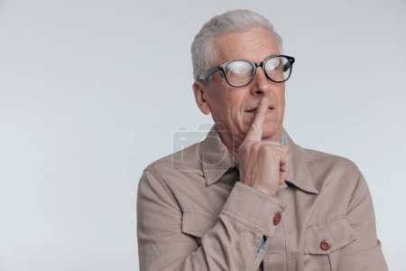 Foto de Anciano reflexivo con chaqueta beige mirando hacia otro lado y pensando en frente de fondo gris - Imagen libre de derechos