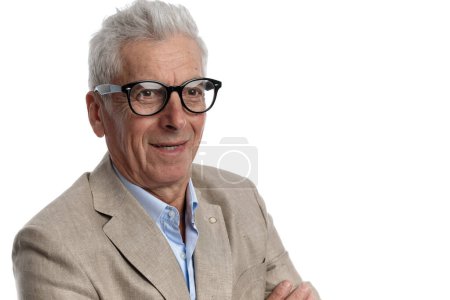 Foto de Picture of handsome guy in his 60s with white hair wearing glasses and looking to side while folding arms on white background in studio - Imagen libre de derechos