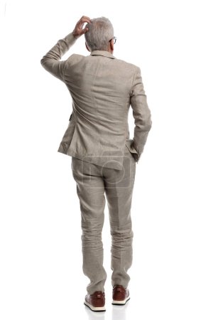 Photo for Confused man with grey hair scratching head and thinking of ways to solve difficult problems while posing with hands in pockets from a back view - Royalty Free Image