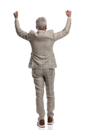 Foto de Back view of old man in his 60s holding arms above head and cheering the victory on white background - Imagen libre de derechos