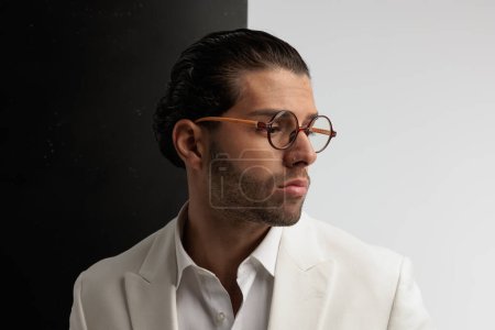 Téléchargez les photos : Portrait d'un bel homme d'affaires regardant vers le côté et posant, debout, portant des lunettes sur fond noir et gris - en image libre de droit