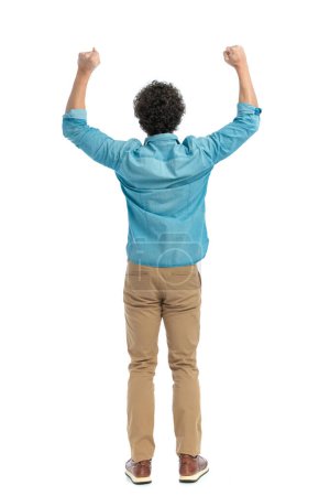 Téléchargez les photos : Back view of curly hair guy holding arms above head and cheering victory in front of white background in studio - en image libre de droit