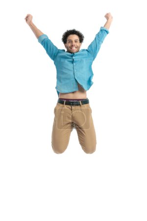 Téléchargez les photos : Dynamic casual man holding arms above head and jumping in the air in front of white background in studio - en image libre de droit