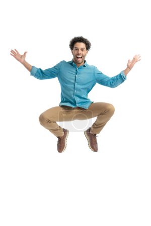 Photo for Enthusiastic man with curly hair jumping in the air and opening arms, being excited and laughing on white background in studio - Royalty Free Image