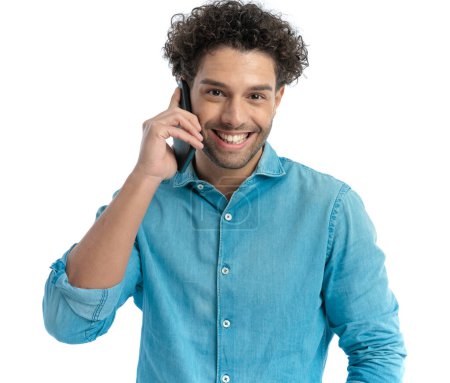 Foto de Excited man with curly hair having a phone conversation and laughing while posing in front of white background in studio - Imagen libre de derechos