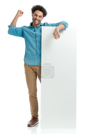 Téléchargez les photos : Full body picture of enthusiastic man showing white board and celebrating victory with fist in the air on white background - en image libre de droit