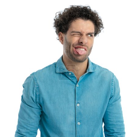 Téléchargez les photos : Funny man with curly hair looking to side and sticking out tongue while posing in a goofy way on white background - en image libre de droit