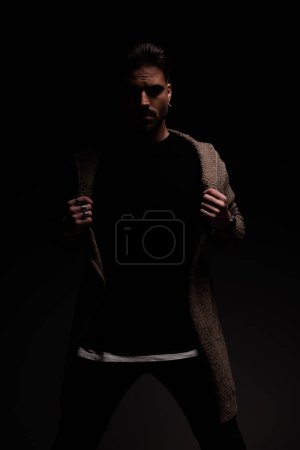 Photo for Portrait of handsome male model fixing his coat with a misteryous vibe, standing, in a fashion pose - Royalty Free Image
