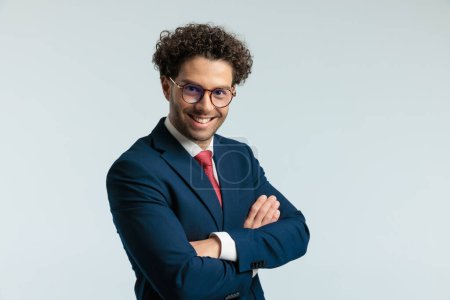Téléchargez les photos : Portrait d'homme d'affaires sexy riant et croisant les bras, debout et portant des lunettes sur fond de studio gris - en image libre de droit