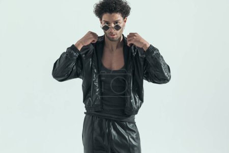 Photo for Young casual man arranging his leather jacket, wearing a leather costume in a fashion pose - Royalty Free Image