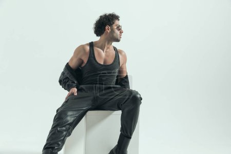 Photo for Young casual man pulling leather jacket off and looking to side, wearing a leather costume in a fashion pose - Royalty Free Image
