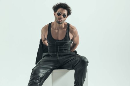 Téléchargez les photos : Handsome casual man undressing himself and showing his muscles, wearing a leather costume in a fashion pose - en image libre de droit
