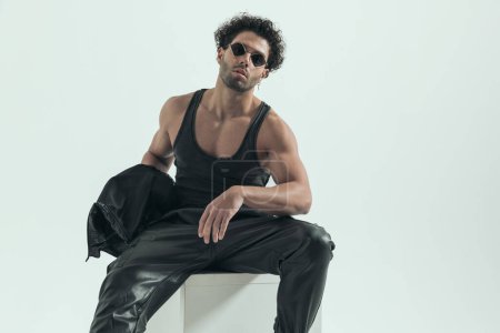 Foto de Attractive casual man taking leather jacket off and showing muscles, wearing a leather costume in a fashion pose - Imagen libre de derechos
