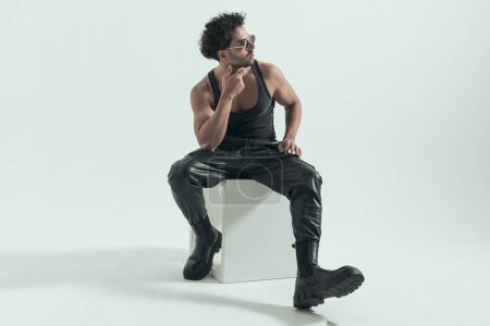 Photo for Sexy casual man rubbing his chin with cool vibe, wearing a leather costume in a fashion pose - Royalty Free Image